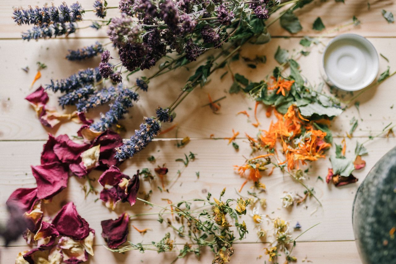 services-01 Assorted dried flowers and herbs scattered on a wooden table with a ceramic bowl.