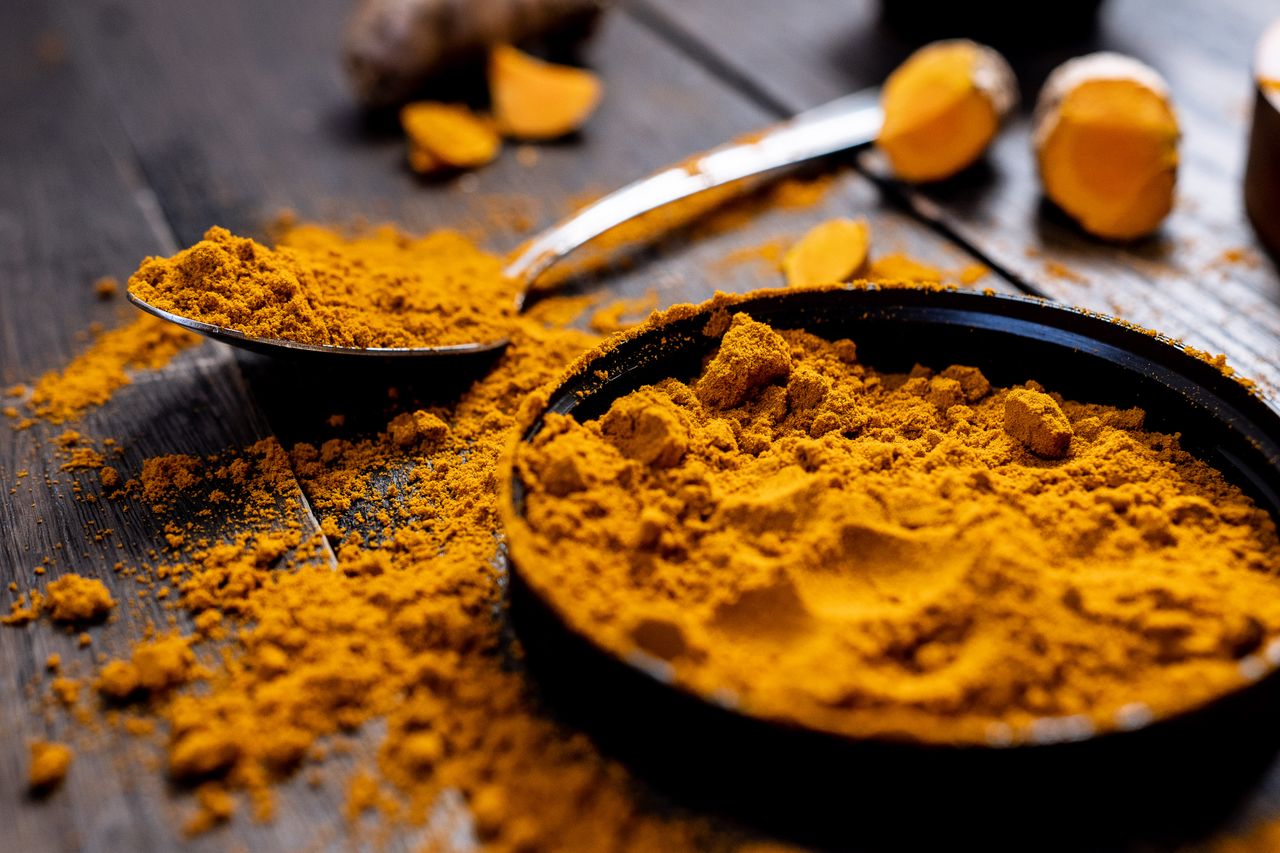 hero-img-02 Close-up of vibrant turmeric powder with root on rustic wooden table, emphasizing texture and color.